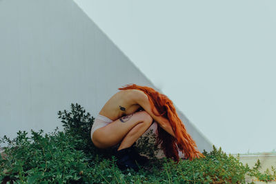 Side view of shirtless woman with redhead crouching on field