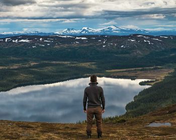 Rear view of man standing on mountain by lake