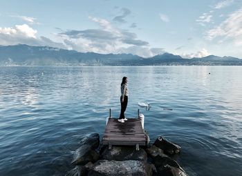 Woman standing on pier over lake against sky