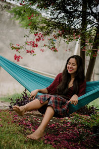 Smiling young woman sitting on hammock against plants