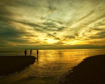 Silhouette people on beach against sky during sunset