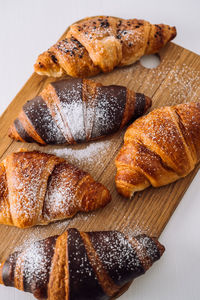 Close up bunch of appetizing brown and chocolate croissants with powdered sugar on a wooden board