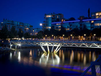 Illuminated bridge over river by buildings in city at night