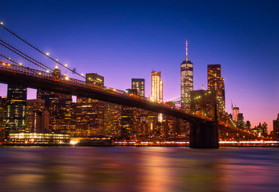 Illuminated bridge over river against buildings at night