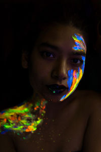 Close-up portrait of young woman with face paint in darkroom