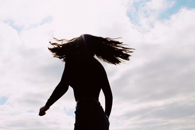 Silhouette woman tossing hair while standing against sky