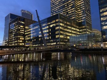 Low angle view of illuminated buildings by river at dusk