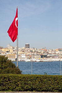 Red flag by river in city against sky