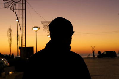 Rear view of silhouette man standing on street against sky during sunset