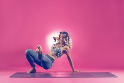 Full length of woman sitting against pink background