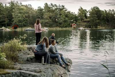 Woman sitting by lake against trees