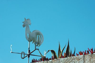 Low angle view of weather vane against clear blue sky on sunny day