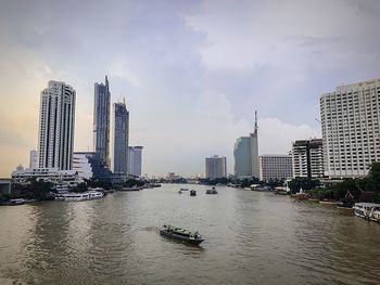 Modern buildings by river against sky in city