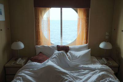 Woman sleeping on bed with sea seen through glass window at home