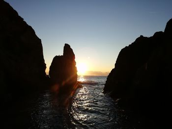 Silhouette rocks in sea against sky during sunset