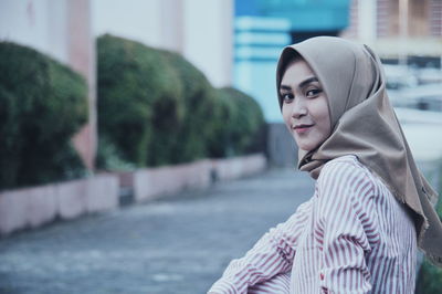 Side view portrait of woman wearing hijab while sitting against buildings