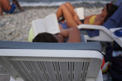 High angle view of people reading books while resting on chairs at beach