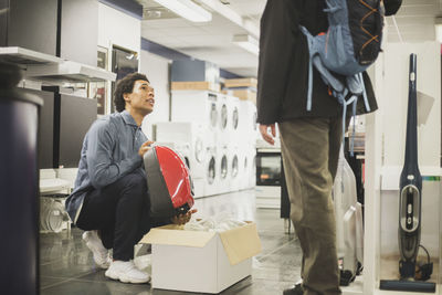 Young salesman showing appliance to male customer in store