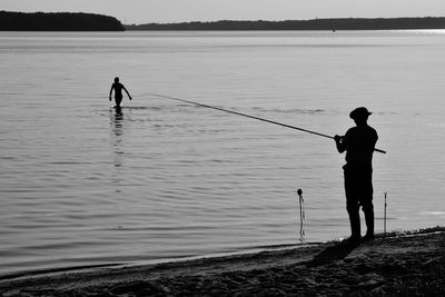 Rear view of silhouette man fishing in river