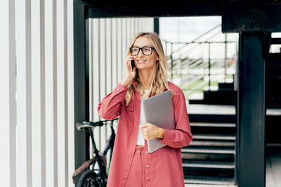 Confident businesswoman speaks on the phone at the exit of the office building.