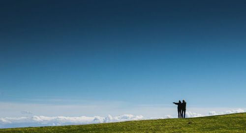 Friends standing on grassy field against blue sky