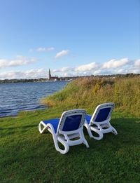 Deck chairs on field by sea against sky