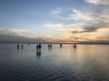 Silhouette people in sea against sky during sunset