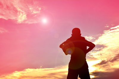 Silhouette boy standing with hands on hips against sky during sunset