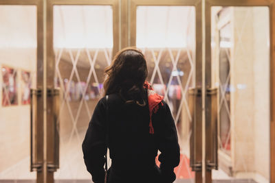 Rear view of woman standing against glass doorway