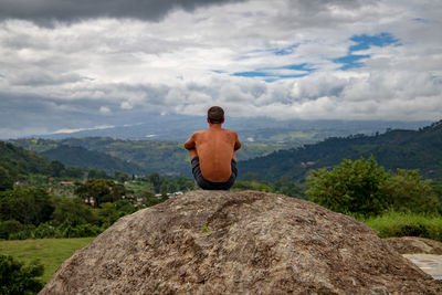 Rear view of shirtless man sitting at mountain against sky