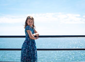 Portrait of girl standing by railing by sea against cloudy sky