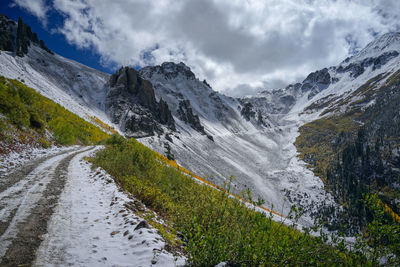 A snow road to mountain with clouds and blue sky with yellow leafs aspen in autumn, colorado.