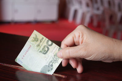 Cropped hand of person putting paper currency into donation box