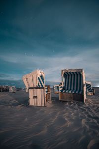 Hooded chairs on beach against sky