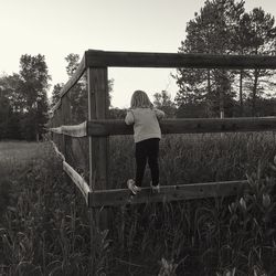 Rear view of boy standing on field against sky