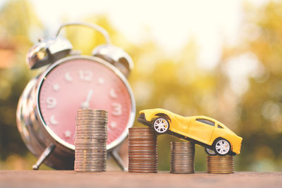 Close-up of alarm clock with stacked coins and toy car on table