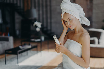 Portrait of young woman holding perfume at home