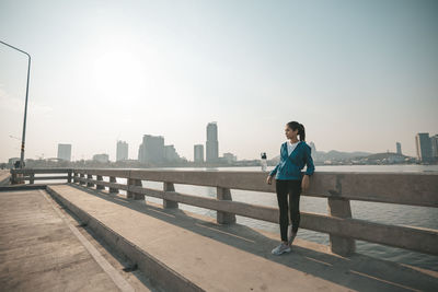 Man standing on railing in city against clear sky