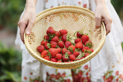 Midsection of woman holding strawberries in wicker basket
