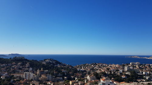 High angle view of townscape by sea against clear blue sky