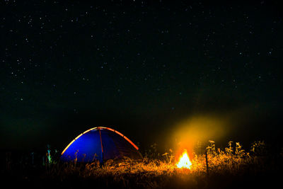 Illuminated tent by campfire against star field at night