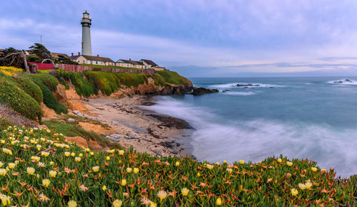 Lighthouse by sea against sky