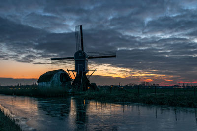 Dutch windmill and old house along a canal after sunset in winter