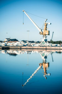 Cranes at harbor against clear blue sky