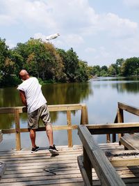 Rear view of man on pier over lake against sky