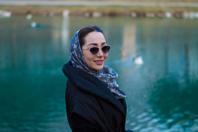 Portrait of young woman wearing sunglasses standing against lake