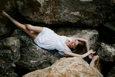 High angle view of happy young woman lying at rocky shore