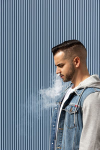 Young man smoking with an electronic cigarette over blue background