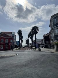 Street amidst palm trees and buildings in city against sky