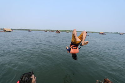 Man looking at friend diving into lake against clear sky